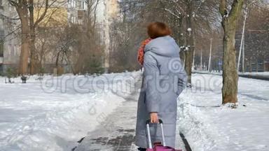 年轻的成年女孩，穿着温暖的外套，穿着五颜六色的针织围巾，走着，拉着她的紫罗兰色的大皮箱。